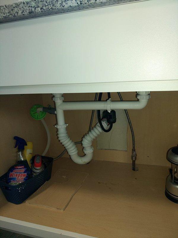 Responded to dual kitchen sink drainage issue in 1942-built home where previous plunging and chemical drain cleaner attempts had failed. Inspected under-sink plumbing configuration, identifying standard white PVC P-trap assembly beneath sink basin. Assessed drainage system for blockages, cleared obstruction in drain line, and restored proper flow to both kitchen sinks. Verified all connections secure and tested drainage performance to ensure complete resolution of backup issue.