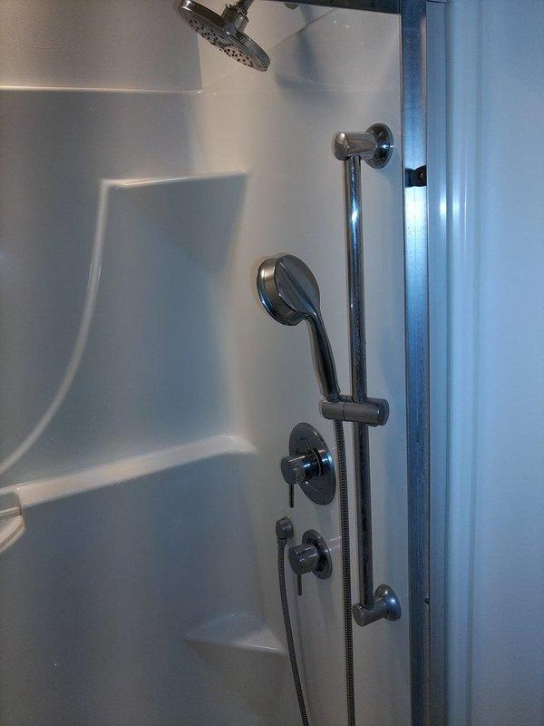 Installed complete dual shower system in existing bathroom, including overhead rain-style showerhead and adjustable slide bar with handheld showerhead assembly. Mounted chrome fixtures to white acrylic shower surround, connected flexible metal hose to water supply, and installed temperature and flow control valves to provide full functionality for the new handheld shower configuration.