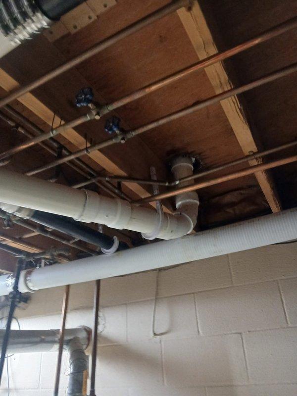 Replaced deteriorated cast iron drain piping in basement with new ABS piping system, connecting to existing cast iron using code-approved banded couplings. Installation included 15 feet of 3-inch pipe, 10 feet of 2-inch pipe, one 3-inch wye cleanout, two 3x2 wyes, one 3x2 cross, one 3-inch closet flange, and miscellaneous 2-inch and 3-inch fittings to complete the drainage system. Additionally, replaced two failed boiler drains within the laundry box to restore proper washing machine hookup functionality. All work completed to code specifications with proper support and alignment of new piping throughout the basement ceiling structure.