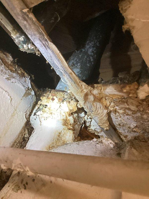 Responded to emergency call for leaking pipe in basement of 99-year-old residential property. Upon arrival, conducted thorough inspection of plumbing system and identified active water leak at deteriorated pipe section in ceiling cavity. Assessment revealed extensive water damage to surrounding drywall and structural materials, with visible discoloration, material separation, and potential mold growth indicating prolonged moisture intrusion. 

Located source of leak at corroded section of supply line showing significant sediment buildup and surface deterioration consistent with age of home's original plumbing infrastructure. Isolated affected water line and performed emergency repair to stop active leak. Evaluated condition of adjacent PVC piping running through ceiling joists, noting accumulation of dirt, dust, and brown staining at pipe intersections. 

Documented all damage with photographs showing extent of deterioration at wall-ceiling junction and condition of exposed plumbing li
