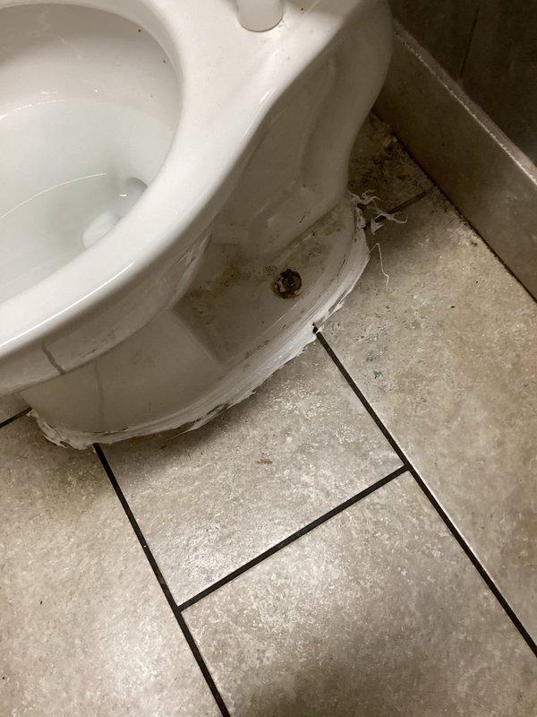 Responded to complaint of raw sewage odor in men's restroom. Upon inspection, discovered significant buildup and contamination around toilet base and floor drain. Toilet exhibited staining and discoloration at floor connection point, indicating potential wax ring failure or seal compromise allowing sewer gases to escape. Floor drain showed heavy sediment accumulation, debris blockage, and signs of dried efflorescence suggesting chronic moisture issues and possible trap seal evaporation. Cleared drain obstruction, flushed system to restore proper trap seal, and sanitized affected areas. Recommended monitoring for recurring odors and consideration of trap primer installation to prevent future dry trap conditions.