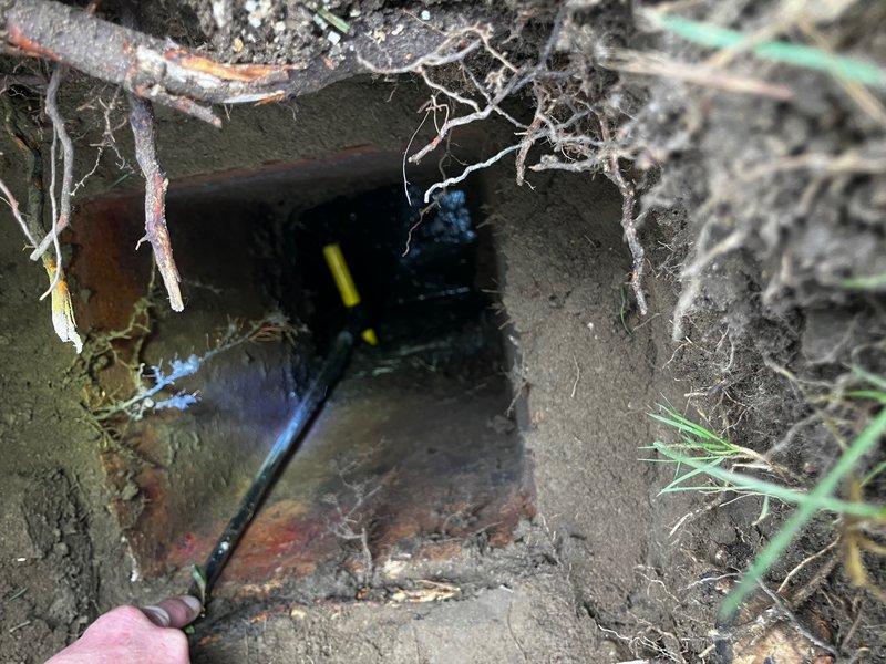 Responded to service call for septic system outlet pipe blockage. Upon arrival, customer had already located and excavated the tank riser and access hatch at the rear of the septic tank. Inspection revealed the liquid level was below the outlet pipe, indicating proper tank function, but the outlet pipe showed signs of obstruction. Visual assessment through the access opening identified potential blockage consisting of accumulated solids or root intrusion within the outlet line. Documented conditions with photographs showing the concrete access structure, exposed outlet piping with visible staining, and surrounding root material near the pipe opening. Recommended drain cleaning services to clear the obstruction and restore proper flow through the outlet line.