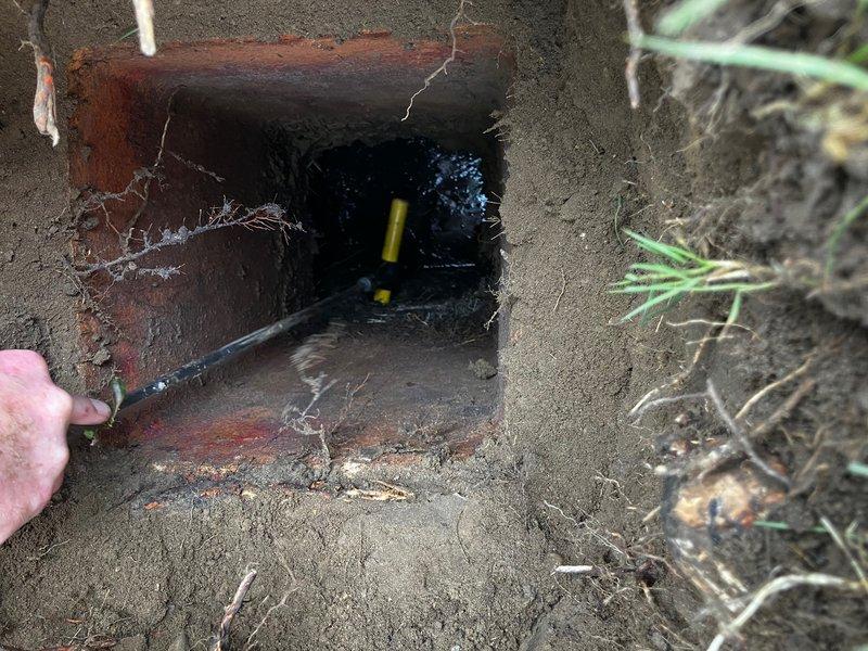 Responded to service call for septic system outlet pipe blockage. Upon arrival, customer had already located and excavated the tank riser and access hatch at the rear of the septic tank. Inspection revealed the liquid level was below the outlet pipe, indicating proper tank function, but the outlet pipe showed signs of obstruction. Visual assessment through the access opening identified potential blockage consisting of accumulated solids or root intrusion within the outlet line. Documented conditions with photographs showing the concrete access structure, exposed outlet piping with visible staining, and surrounding root material near the pipe opening. Recommended drain cleaning services to clear the obstruction and restore proper flow through the outlet line.
