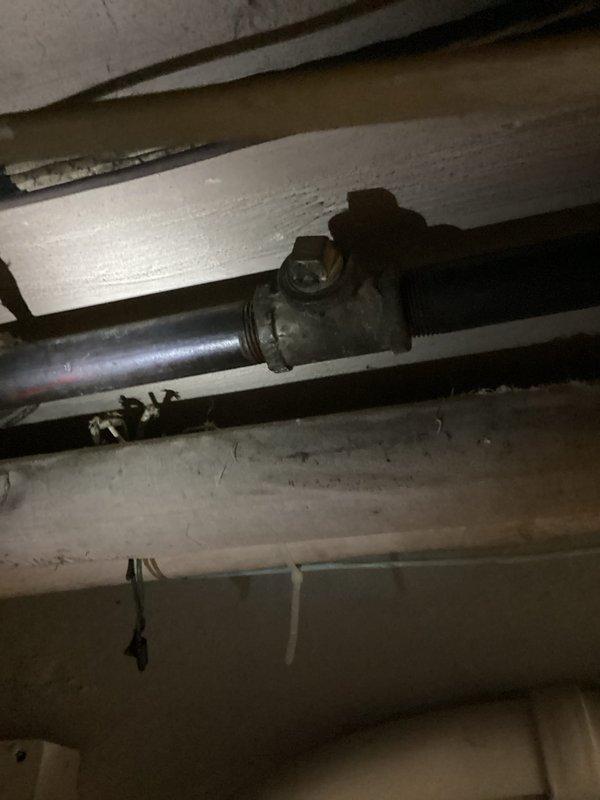 Responded to service call for natural gas line installation to generator. Located existing gas supply line in basement/crawl space area with shut-off valve on galvanized pipe system. Tapped into main gas line and extended new gas piping from basement location to exterior generator unit positioned near foundation. Routed gas line through foundation to reach standby generator equipment located outside on brick paver surface adjacent to cream-colored vinyl siding. Installed appropriate fittings and connections to ensure proper gas supply to generator. Verified all connections were secure and system was ready for pressure testing and final inspection.