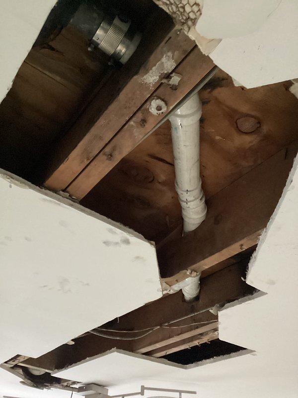Accessed bathtub drainage system through kitchen ceiling below to address failing waste line. Removed section of ceiling drywall to expose plumbing infrastructure and structural framing. Replaced complete bathtub drain line from tub shoe assembly to connection point at main drain stack using new PVC piping. Secured all new plumbing components to wooden joists with appropriate brackets and fasteners per code requirements. System tested and verified for proper drainage flow and leak-free operation.