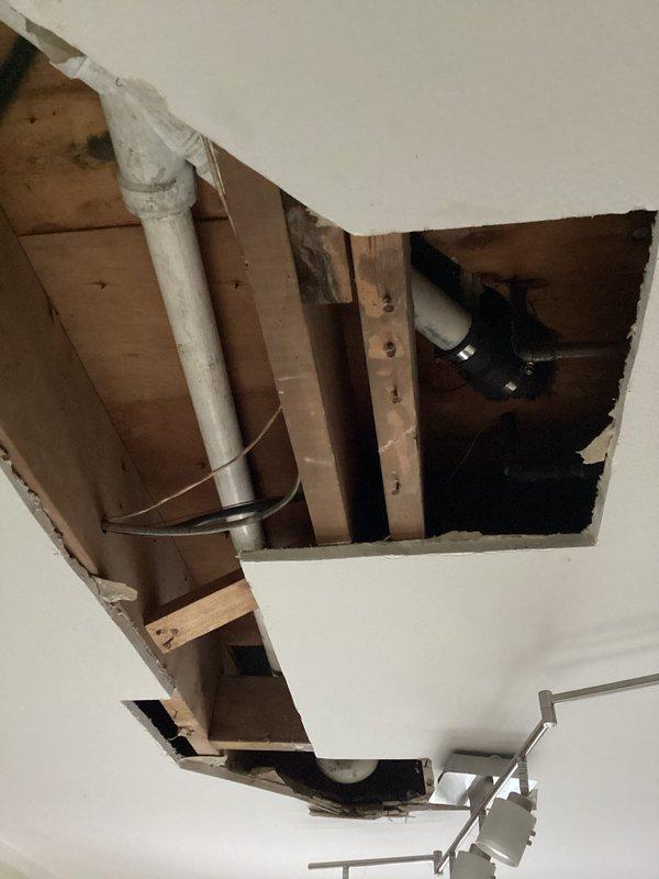 Accessed bathtub drainage system through kitchen ceiling below to address failing waste line. Removed section of ceiling drywall to expose plumbing infrastructure and structural framing. Replaced complete bathtub drain line from tub shoe assembly to connection point at main drain stack using new PVC piping. Secured all new plumbing components to wooden joists with appropriate brackets and fasteners per code requirements. System tested and verified for proper drainage flow and leak-free operation.