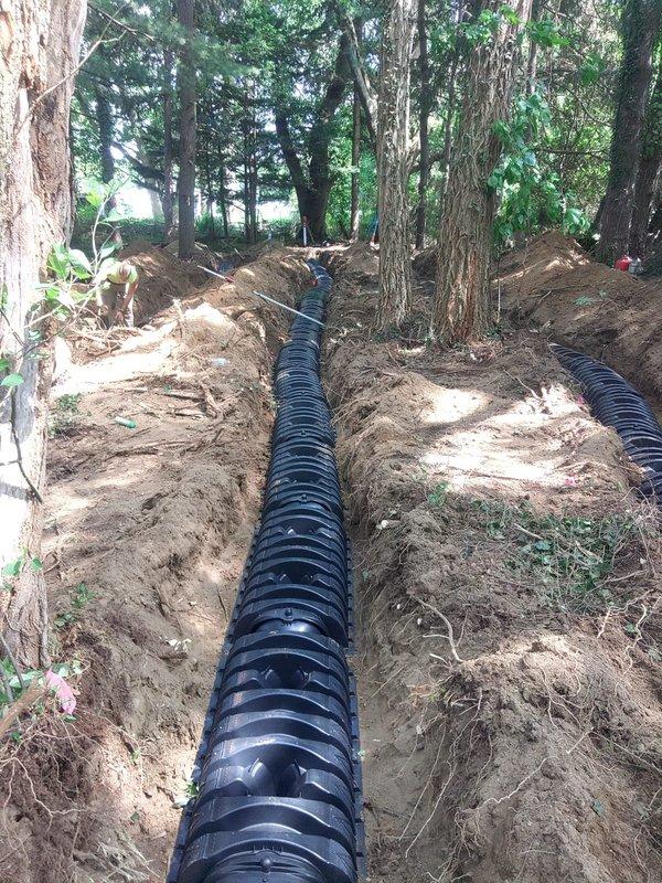 Completed installation of new septic drainage system in wooded residential area, excavating two parallel trenches and installing black corrugated drainage pipes for proper waste water dispersion. Coordinated site access with on-site occupant and worked alongside electrical contractor to ensure proper system integration and functionality.