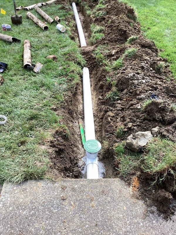 Excavated trench through residential lawn from front left downspout to existing storm sewer main, crossing city sidewalk. Removed deteriorated original drainage pipes that were no longer functioning properly. Installed approximately 60 feet of new 4-inch PVC drain line through excavated trench, ensuring proper grade and alignment for optimal water flow. Reconnected new drainage system to downspout at origin point and tied into existing storm sewer main at terminus. Backfilled trench with excavated soil and compacted as necessary. Original concrete sidewalk and finish landscaping restoration not included in scope of work.
