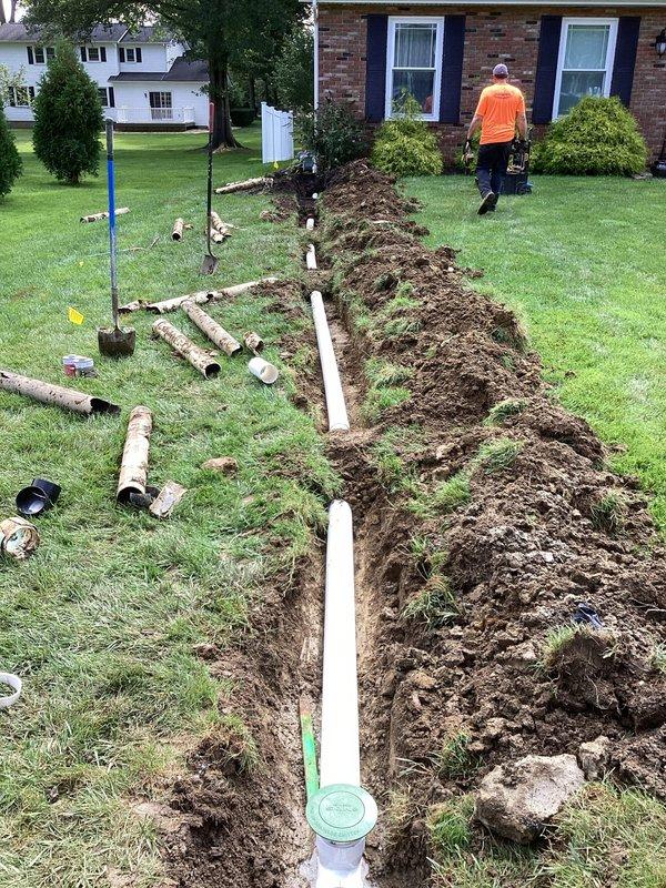 Excavated trench through residential lawn from front left downspout to existing storm sewer main, crossing city sidewalk. Removed deteriorated original drainage pipes that were no longer functioning properly. Installed approximately 60 feet of new 4-inch PVC drain line through excavated trench, ensuring proper grade and alignment for optimal water flow. Reconnected new drainage system to downspout at origin point and tied into existing storm sewer main at terminus. Backfilled trench with excavated soil and compacted as necessary. Original concrete sidewalk and finish landscaping restoration not included in scope of work.