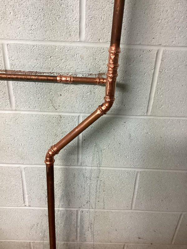Responded to copper pipe leak in building's plumbing system. Located and assessed the leak point in the copper piping configuration mounted against the interior cinder block wall. Repaired the compromised copper pipe section by addressing the failed solder joint, ensuring proper water-tight seal and restoring full system integrity. Verified all connections and tested the system to confirm no additional leaks were present.