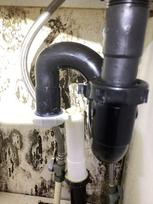 Responded to bathroom sink leak complaint and performed inspection of under-sink plumbing assembly. Upon arrival, accessed upper unit using provided lockbox and investigated the drainage system. Found extensive water damage, mold growth, and deterioration on cabinet surfaces and wall areas surrounding the plumbing fixtures, indicating chronic moisture intrusion. The P-trap, drain assembly connections, and supply lines were examined for leaks and proper sealing. Documented existing conditions with photographs showing significant discoloration patterns on cabinet floor and wall surfaces, along with the configuration of black P-trap, white PVC drainage pipes, braided metal supply line, and disposal connection with hose clamp. All plumbing components and connection points were assessed for integrity and proper function to identify the source of reported leaking during sink use.