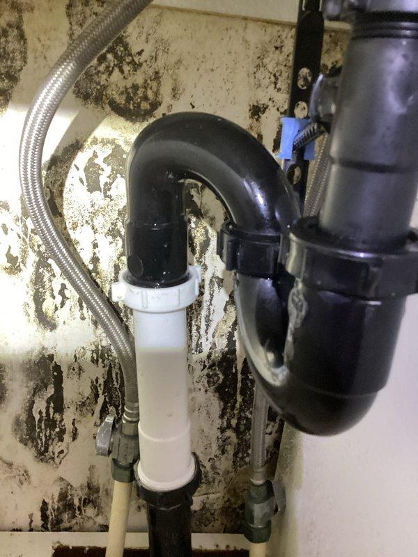 Responded to bathroom sink leak complaint and performed inspection of under-sink plumbing assembly. Upon arrival, accessed upper unit using provided lockbox and investigated the drainage system. Found extensive water damage, mold growth, and deterioration on cabinet surfaces and wall areas surrounding the plumbing fixtures, indicating chronic moisture intrusion. The P-trap, drain assembly connections, and supply lines were examined for leaks and proper sealing. Documented existing conditions with photographs showing significant discoloration patterns on cabinet floor and wall surfaces, along with the configuration of black P-trap, white PVC drainage pipes, braided metal supply line, and disposal connection with hose clamp. All plumbing components and connection points were assessed for integrity and proper function to identify the source of reported leaking during sink use.