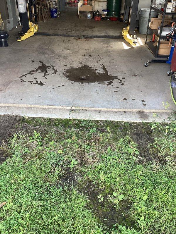 Responded to drainage backup issue in garage with three floor drains, two experiencing severe blockage and standing water accumulation. Upon arrival, identified chronic moisture problem at rear of garage area with visible water staining on concrete floor. Assessed drainage system serving automotive service bay, noting oil and fluid contamination on floor surfaces that may be contributing to drain line buildup. Inspected all three drain locations and determined primary blockage points affecting water evacuation from work area.
