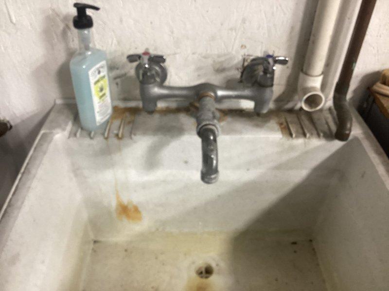 Responded to warehouse facility for leaking faucet at utility sink. Upon inspection, found aged chrome dual-handle faucet assembly with visible wear and corrosion on mounting hardware. Identified leak originating from faucet valve stem area. Disassembled faucet assembly, replaced worn valve stem washers and packing, and reassembled unit. Tested both hot and cold water valves under full pressure to confirm proper operation and verified no active leaks. Sink drainage confirmed functional with no secondary issues noted.