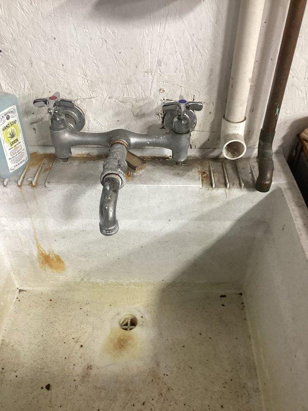 Responded to warehouse facility for leaking faucet at utility sink. Upon inspection, found aged chrome dual-handle faucet assembly with visible wear and corrosion on mounting hardware. Identified leak originating from faucet valve stem area. Disassembled faucet assembly, replaced worn valve stem washers and packing, and reassembled unit. Tested both hot and cold water valves under full pressure to confirm proper operation and verified no active leaks. Sink drainage confirmed functional with no secondary issues noted.