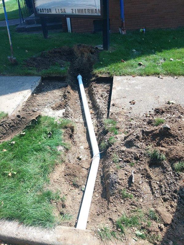 Excavated trench adjacent to sidewalk to expose existing 4" Schedule 40 PVC drain line running to curb outlet. Removed damaged section of pipe and installed approximately 8 feet of Schedule 35 PVC pipe to complete repair. Backfilled excavation area with Type 57 stone; concrete restoration to be completed by property owner.