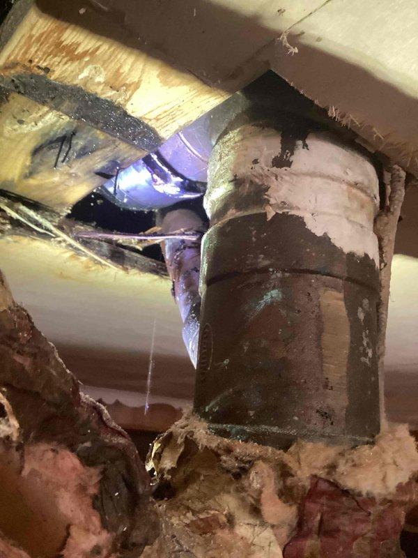 Responded to water leak originating from vertical pipe running from basement to roof. Upon arrival, accessed ceiling cavity in basement area where ceiling material had been removed to expose plumbing infrastructure. Located source of leak at corroded copper pipe fitting in crawl space area between floor joists. Copper fitting exhibited significant verdigris buildup and oxidation, indicating prolonged moisture exposure and material deterioration. Documented condition of affected plumbing components, including multiple sections of copper piping showing corrosion. Photographed exposed HVAC ductwork visible through ceiling opening and surrounding water-damaged structural elements. Ceiling drywall had been cut away to facilitate access to leaking pipe assembly, revealing darkened wooden framing members consistent with moisture intrusion. Assessed extent of water damage to surrounding building materials and insulation.