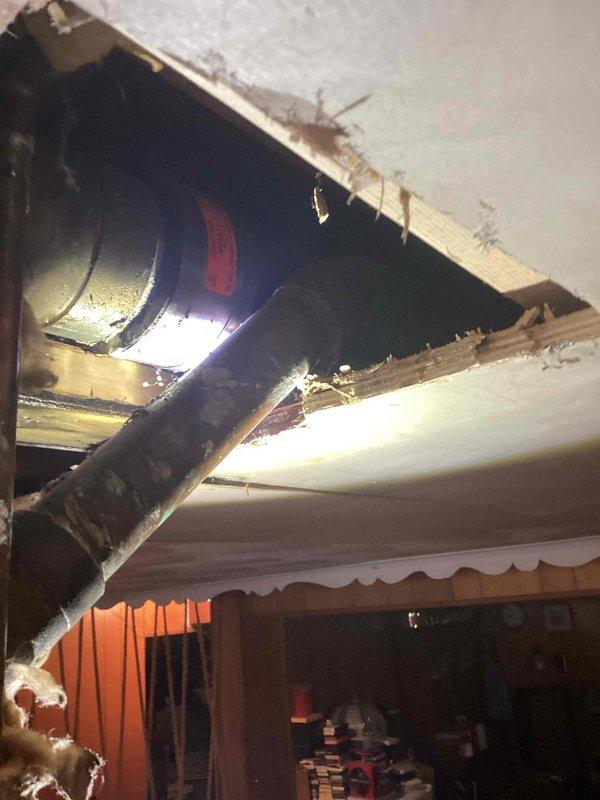 Responded to water leak originating from vertical pipe running from basement to roof. Upon arrival, accessed ceiling cavity in basement area where ceiling material had been removed to expose plumbing infrastructure. Located source of leak at corroded copper pipe fitting in crawl space area between floor joists. Copper fitting exhibited significant verdigris buildup and oxidation, indicating prolonged moisture exposure and material deterioration. Documented condition of affected plumbing components, including multiple sections of copper piping showing corrosion. Photographed exposed HVAC ductwork visible through ceiling opening and surrounding water-damaged structural elements. Ceiling drywall had been cut away to facilitate access to leaking pipe assembly, revealing darkened wooden framing members consistent with moisture intrusion. Assessed extent of water damage to surrounding building materials and insulation.