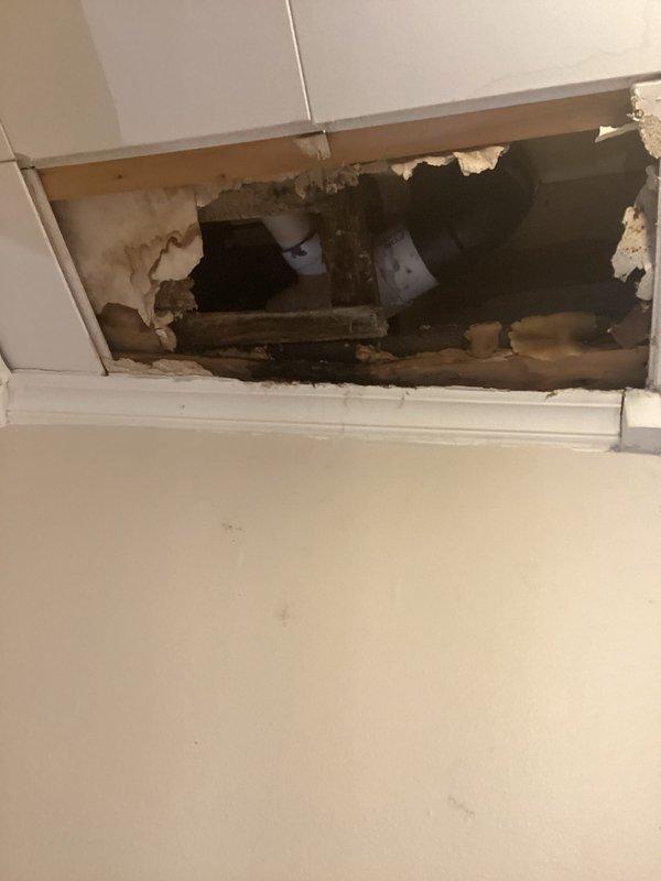 Responded to emergency water leak in bathroom with water penetrating through ceiling to lower level. Upon arrival, performed exploratory demolition of ceiling drywall and wall sections to locate source of active leak. Removed damaged drywall panels at ceiling corner and adjacent wall area, exposing wooden framing members, joists, and plumbing infrastructure. Investigation revealed multiple plumbing fixtures or supply lines within bathroom causing water intrusion. Documented extent of water damage to structural wood members showing visible moisture staining and discoloration. Identified compromised PVC piping and other plumbing components within ceiling cavity requiring repair. Photographed exposed conditions for insurance documentation and repair planning.