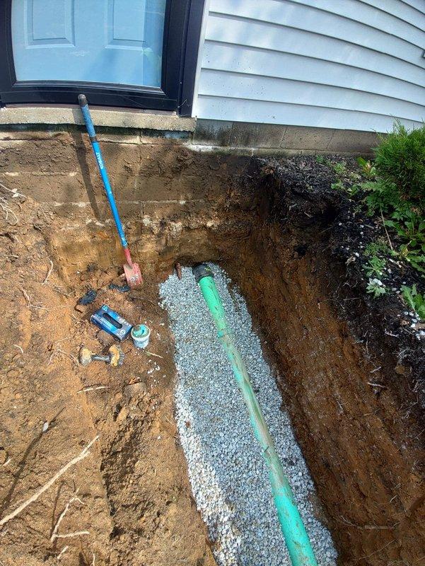 Completed full sewer lateral replacement from house foundation to main line connection. Excavated trench alongside foundation, removed old deteriorated sewer pipe, and installed new green PVC sewer line properly bedded in crushed stone for optimal drainage and support. All excavation work completed with proper depth and grade to ensure gravity flow, pipe secured with appropriate couplings, and system tested for proper function prior to backfill.