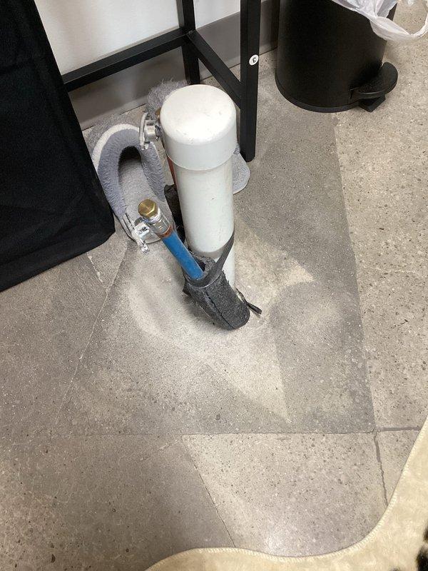 Responded to commercial customer inquiry regarding 2-inch drain and PEX pipe installation protruding through floor. Customer requested assessment and estimate for cutting out 12x12-inch section of flooring and installing floor box to conceal plumbing connections. Documented existing installation with photographs showing copper piping with brass fittings and white cylindrical component with blue flex line connection on gray tile floor. Forwarded inquiry and documentation to management for feasibility review and pricing determination.