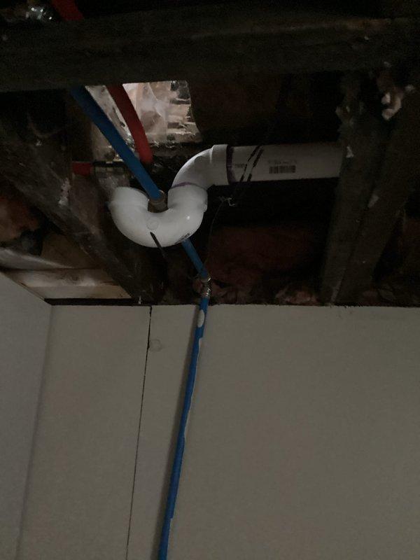Completed pre-inspection callback to verify previously installed plumbing work. Documented PVC drain line installation with proper purple primer application, confirmed hot and cold water supply line routing through floor penetration, and photographed ceiling cavity showing insulated water lines and proper pipe support in preparation for municipal inspection.