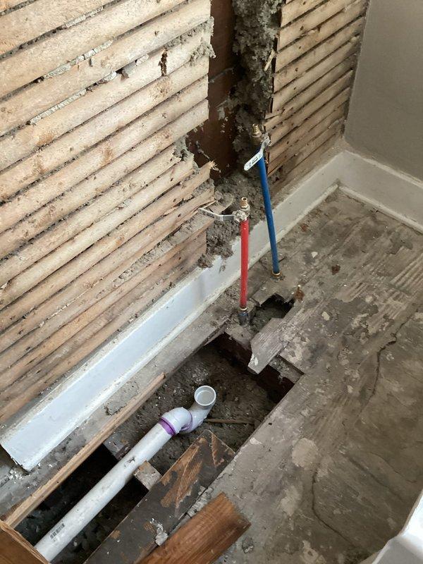 Completed pre-inspection callback to verify previously installed plumbing work. Documented PVC drain line installation with proper purple primer application, confirmed hot and cold water supply line routing through floor penetration, and photographed ceiling cavity showing insulated water lines and proper pipe support in preparation for municipal inspection.