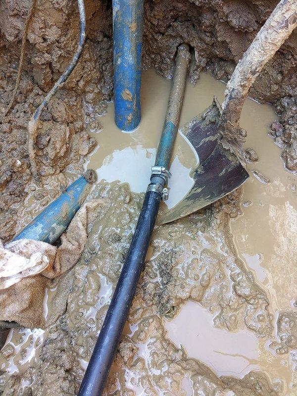 Excavated front yard water main to locate and repair underground break extending approximately 14 feet from street entry point. Exposed multiple pipe sections including deteriorated water service line with visible coupling failure. Replaced damaged section with new blue PVC piping and secure fittings to restore water service. Worked in challenging wet conditions with standing groundwater present throughout excavation. Backfilled trench and restored yard surface upon completion of repairs.
