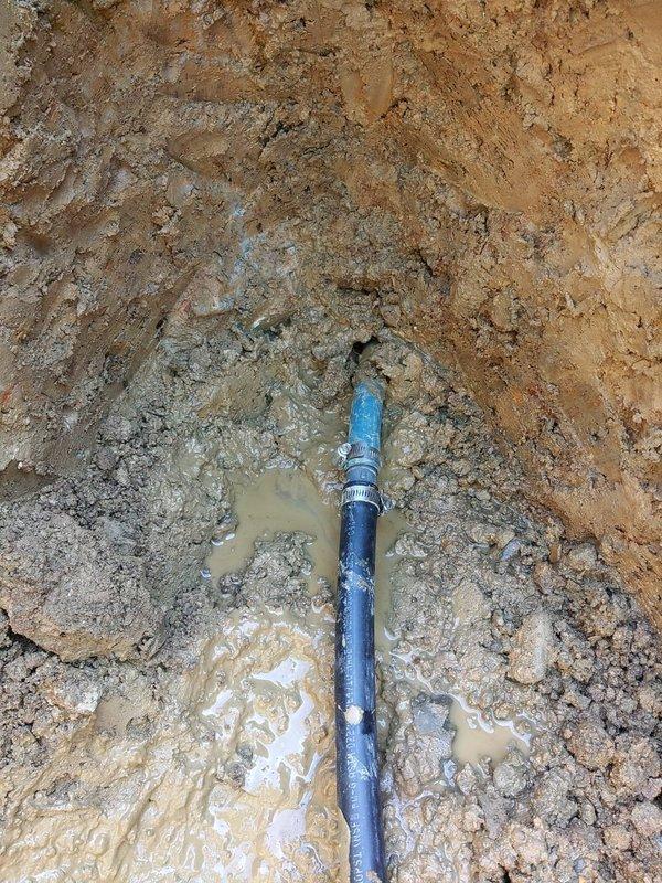 Excavated front yard water main to locate and repair underground break extending approximately 14 feet from street entry point. Exposed multiple pipe sections including deteriorated water service line with visible coupling failure. Replaced damaged section with new blue PVC piping and secure fittings to restore water service. Worked in challenging wet conditions with standing groundwater present throughout excavation. Backfilled trench and restored yard surface upon completion of repairs.