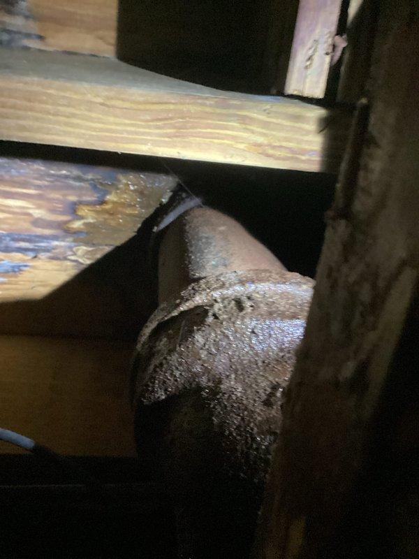 Responded to a leak originating from the upstairs bathroom that was seeping through to the downstairs bathroom, with water damage visible beneath the bathroom cabinet. Inspected the affected areas and documented the water intrusion points, including compromised pipe penetrations through the floor structure and insulated plumbing lines in the ceiling cavity. Photographed the damaged areas showing deteriorated sealing material around pipe penetrations and the HVAC ductwork or plumbing system running through the wooden framing members.