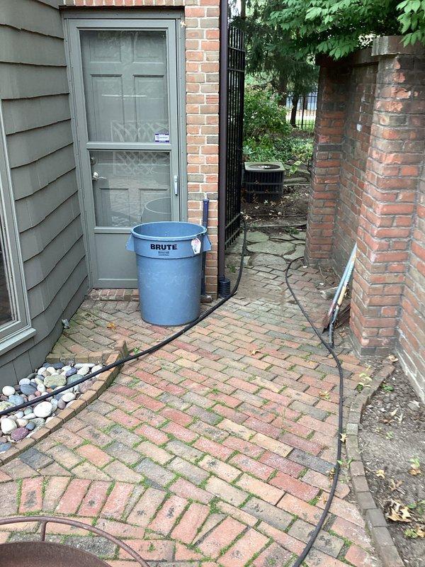 Performed camera inspection of exterior downspout drainage system as requested. Deployed inspection equipment through accessible downspout locations on brick exterior and side yard areas to assess underground drainage line condition and flow path. Documentation captured showing patio area with significant moss growth on pavers and side yard access point with brick paving, confirming proper camera line deployment and completion of requested drainage system evaluation.