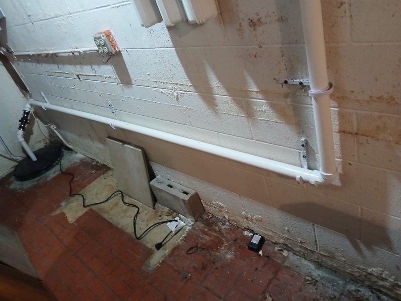 Installed new 1/2 HP sump pump in basement with basin and rerouted discharge line through crawlspace using PVC pipe and fittings. Excavated and installed 4" SDR35 solid PVC pipe for new drainage system, connecting sump pump discharge and three gutter downspouts to existing 4" line near detached garage. All piping secured with proper mounting brackets and fittings, creating complete drainage solution for foundation water management.