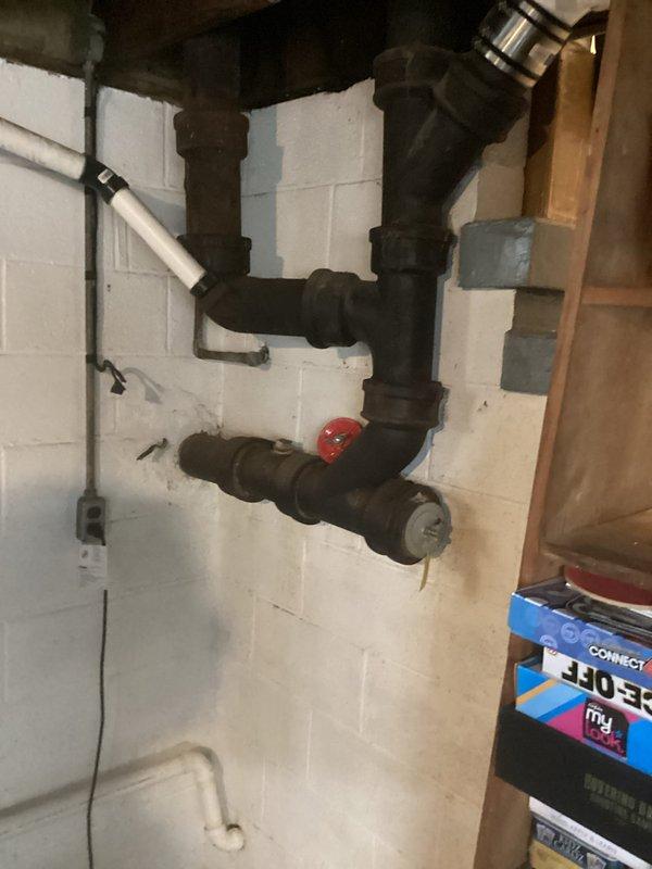 Responded to service call for busted pipe assessment. Upon arrival, inspected aging cast iron/steel plumbing assembly mounted on basement cinder block wall, identifying deteriorated pipe sections with visible corrosion and oxidation. Documented existing plumbing configuration including multiple joints, fittings, and red-handled valve for estimate preparation. Photographed damaged areas and surrounding pipe infrastructure to provide comprehensive visual documentation for repair proposal.
