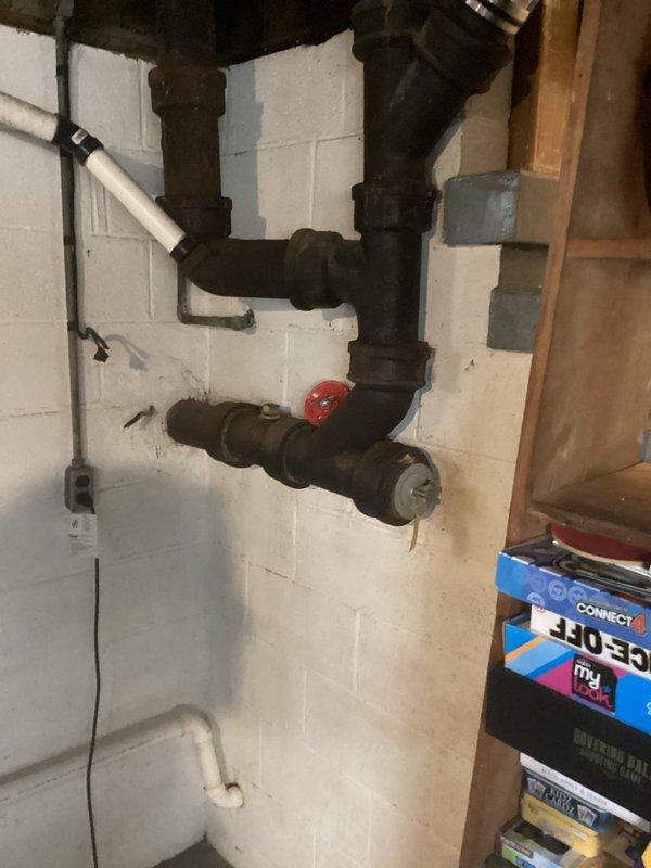 Responded to service call for busted pipe assessment. Upon arrival, inspected aging cast iron/steel plumbing assembly mounted on basement cinder block wall, identifying deteriorated pipe sections with visible corrosion and oxidation. Documented existing plumbing configuration including multiple joints, fittings, and red-handled valve for estimate preparation. Photographed damaged areas and surrounding pipe infrastructure to provide comprehensive visual documentation for repair proposal.