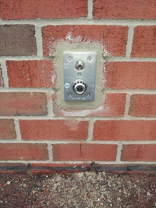 Installed a new outdoor Ecolotrol frost-free faucet by removing interior wall bricks to access the masonry opening and the copper supply line. Connected the copper supply with a press fitting, then mounted the stainless steel wall plate and sealed it into the brick wall with mortar. Used a shop vac to contain dust and debris during the work.