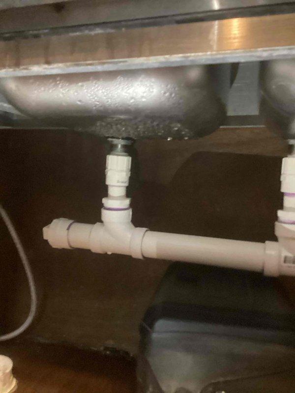 Responded to a reported leak at a restroom double-basin stainless steel sink that was allowing water to migrate through the ceiling below. Inspected the under-sink drain assembly, including the basket strainer connections, tee fitting, and slip-joint connectors, and identified moisture and condensation at the basin underside and drain junctions as the source. Serviced the drain assembly to eliminate the leak, restoring proper function and preventing further water intrusion to the area below.