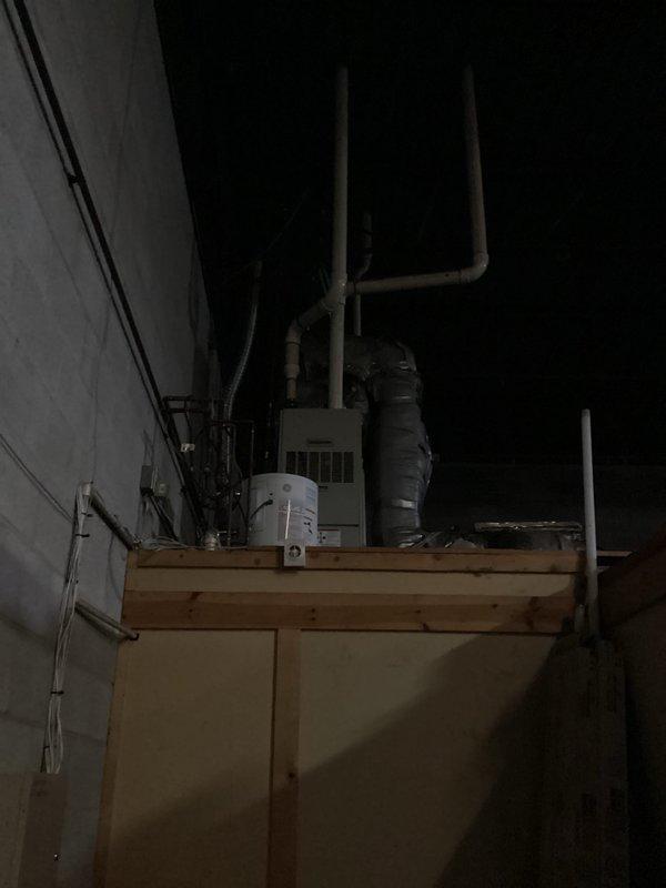 Conducted site evaluation of commercial HVAC system with Comfortmaker furnace located in loft/attic space mounted on wooden platform with connected ductwork and PVC venting. Roof-mounted AC unit was not directly accessible during inspection. Documented current installation configuration including GE water heater proximity and existing ductwork condition to prepare comprehensive replacement estimate.