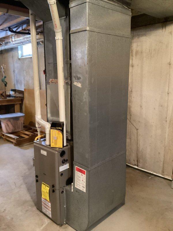 Conducted assessment for furnace replacement quote on 12-year-old unit located in unfinished basement of residential property. Existing system features standard PVC venting and is positioned against concrete wall with nearby ductwork connections. Documented current installation configuration to prepare accurate replacement options for homeowner.