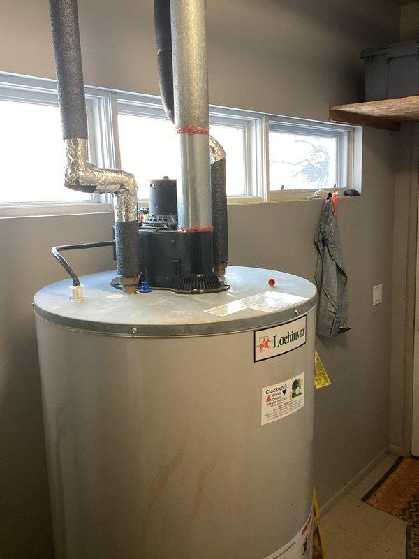 Conducted comprehensive HVAC replacement estimate for existing system featuring a Lochinvar water heater showing signs of wear (visible water stains on exterior) and an adjacent dark gray mechanical unit with PVC and copper pipe connections. Documented current installation configuration including ventilation ducting, insulation, and plumbing connections to provide accurate replacement options.