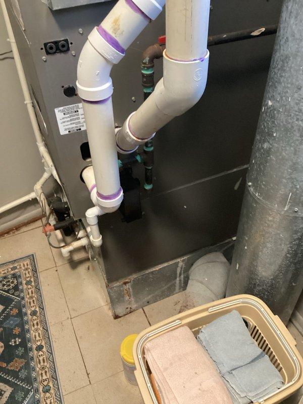 Conducted comprehensive HVAC replacement estimate for existing system featuring a Lochinvar water heater showing signs of wear (visible water stains on exterior) and an adjacent dark gray mechanical unit with PVC and copper pipe connections. Documented current installation configuration including ventilation ducting, insulation, and plumbing connections to provide accurate replacement options.