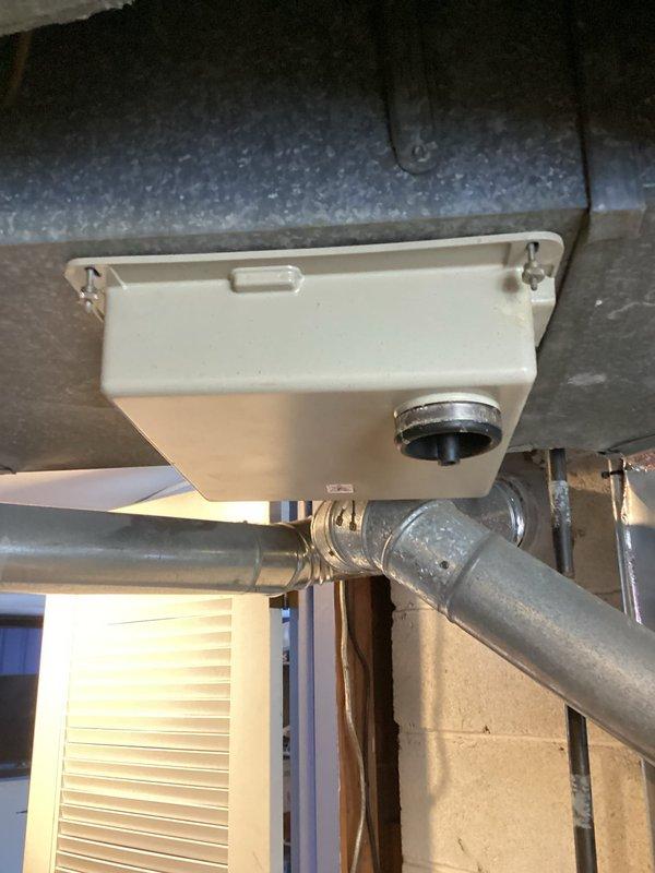 Performed assessment of aging HVAC system (9-11 years old) for potential replacement. Inspected existing ductwork configuration, including galvanized steel ducts with elbow joints mounted along concrete block wall. Evaluated condensate drainage system with white drain box and associated piping. Documentation included photographs of critical system components to support replacement recommendation due to equipment age.