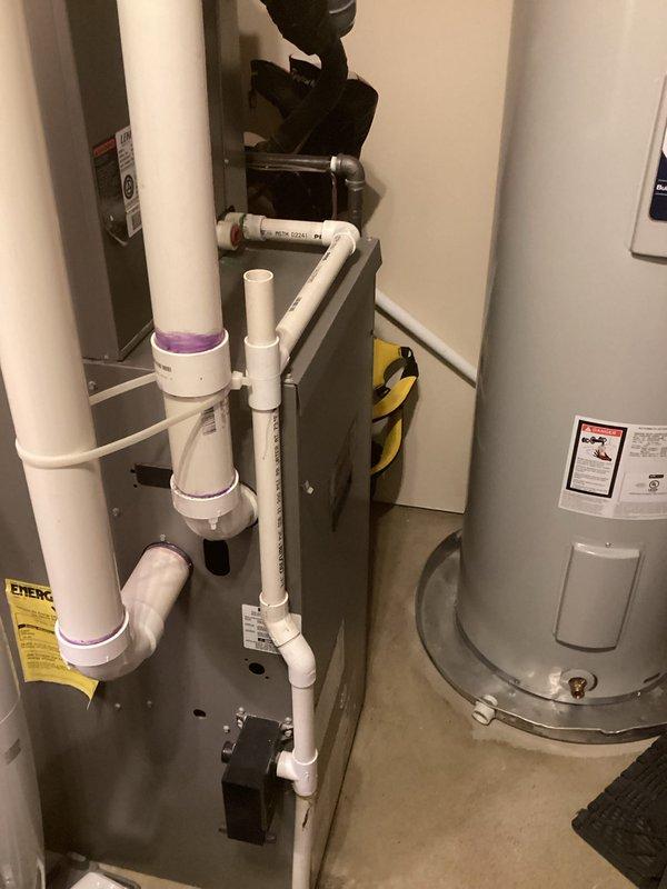 Conducted comprehensive assessment of residential HVAC system for potential replacement. Inspected existing furnace/air handler unit with connected PVC drainage system and condensate trap, noting energy efficiency ratings. Evaluated adjacent water heater installation and examined secondary equipment components including secured cylindrical element with retention straps and associated pipe fittings.
