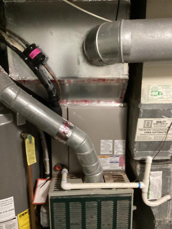 Completed HVAC system replacement estimate for a residential property, documenting the existing furnace unit with connected ductwork, PVC drainage, and ventilation components in a utility room that doubles as storage space. Photos were taken of the complete system installation showing the furnace with information labels, metal ductwork connections, and the overall configuration to support accurate replacement planning.