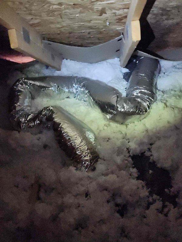 Performed inspection of bathroom exhaust fan reported to be making unusual noise. Accessed attic crawlspace to examine fan unit and ductwork. Located metal HVAC ducting wrapped in reflective insulation with disturbed fiberglass insulation surrounding the area. Identified debris blockage in fan housing causing operational noise, cleared obstruction and verified proper functionality before completing service.