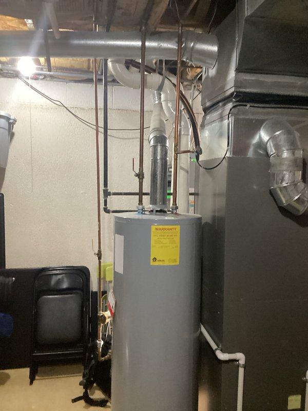 Conducted site assessment for water heater replacement quote. Documented existing system consisting of a cylindrical tank with copper supply lines and PVC drainage piping in utility room with adjacent HVAC equipment. Photographed installation area to develop accurate replacement specifications.