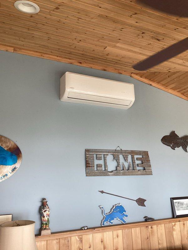 Completed estimate for mini-split installation featuring an interior wall-mounted Lennox ductless air handler in client's cabin-style room and corresponding exterior condenser unit mounted on metal support legs with proper electrical connections. System was properly installed with line sets routed through exterior wall, with condenser positioned on decorative river rock landscaping area.