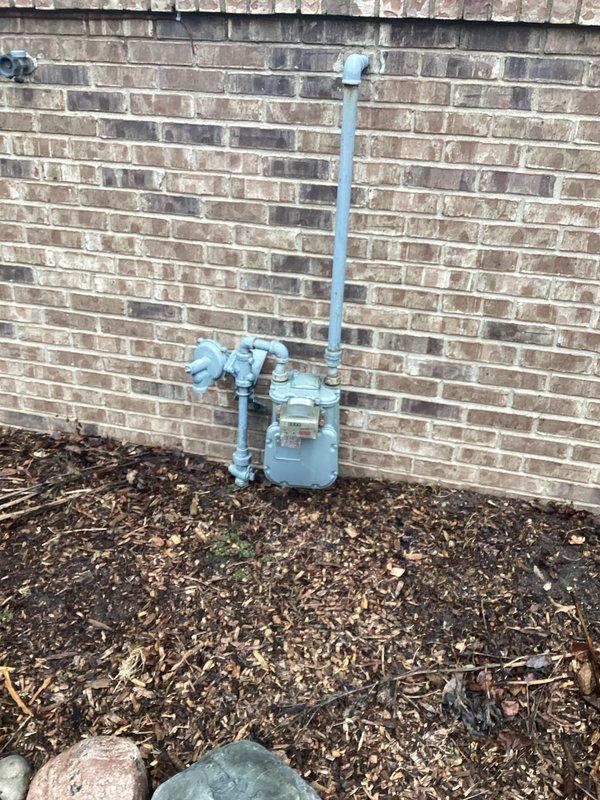 Performed generator installation assessment at residential property. Evaluated natural gas meter capacity and connection options on exterior brick wall for potential generator fuel supply. Inspected two electrical panels mounted on plywood wall, noting available breaker spaces and existing circuit configuration for proper generator integration.