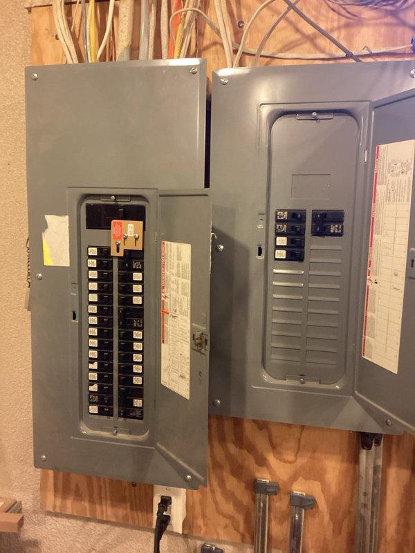 Performed generator installation assessment at residential property. Evaluated natural gas meter capacity and connection options on exterior brick wall for potential generator fuel supply. Inspected two electrical panels mounted on plywood wall, noting available breaker spaces and existing circuit configuration for proper generator integration.