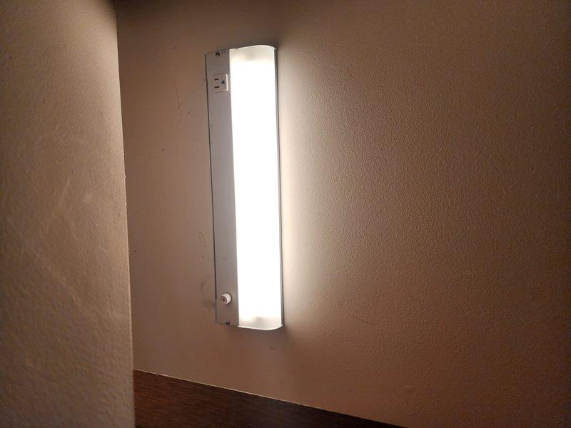 Successfully installed two light fixtures - a fluorescent wall-mounted unit in bathroom/kitchen area near decorative tile work and GFCI outlet, and a rectangular LED fixture on textured wall in hallway/corner location. Additionally installed Ring camera system as requested, ensuring proper mounting and functionality.
