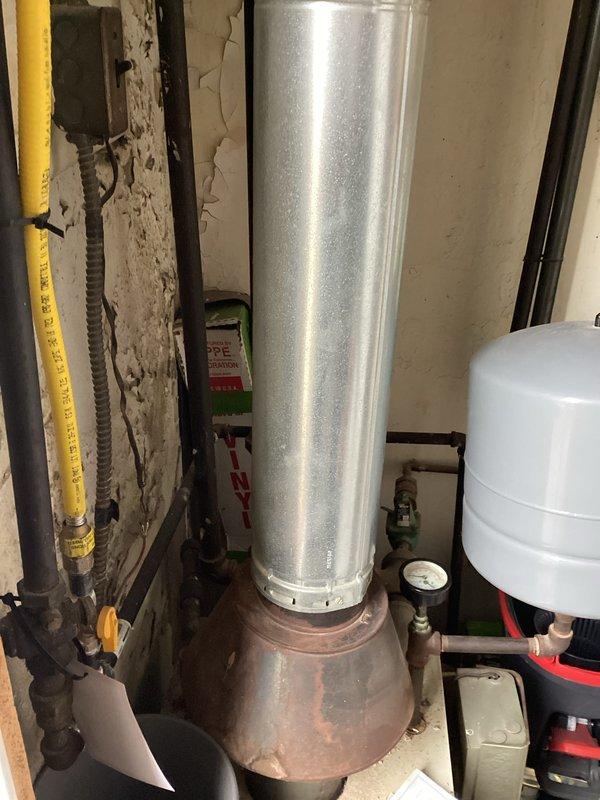 Conducted boiler assessment in commercial building's utility room, documenting significant wall deterioration around existing hot water system. Inspection revealed aging boiler components including deteriorated flue pipe, expansion tank connections, and gas line installation. Photographed exposed ductwork and framing requiring attention during potential replacement. Recommended comprehensive system upgrade due to extensive structural damage and aged equipment condition.